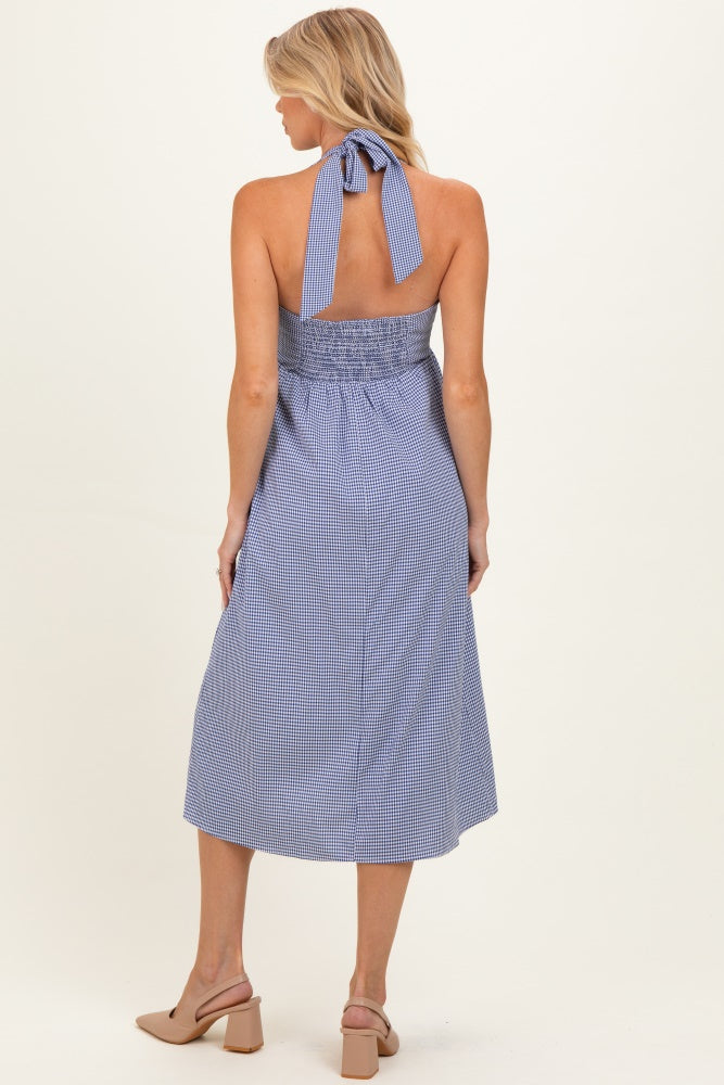 woman wearing a blue and white gingham maternity dress with a halter neck and smocked back, showing her baby bump