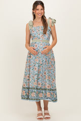 woman wearing a floral print maternity dress with bow straps and a baby bump visible, standing and smiling