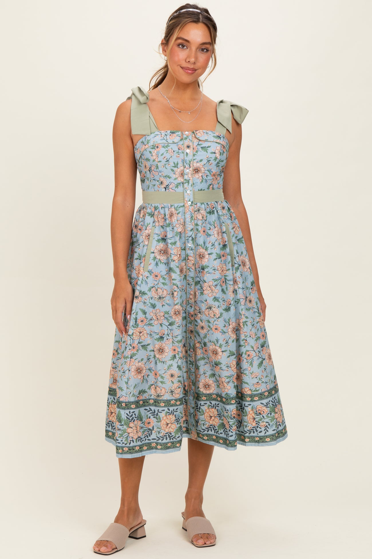 woman wearing a floral print midi dress with green ribbon straps and a fitted bodice, styled with slide sandals