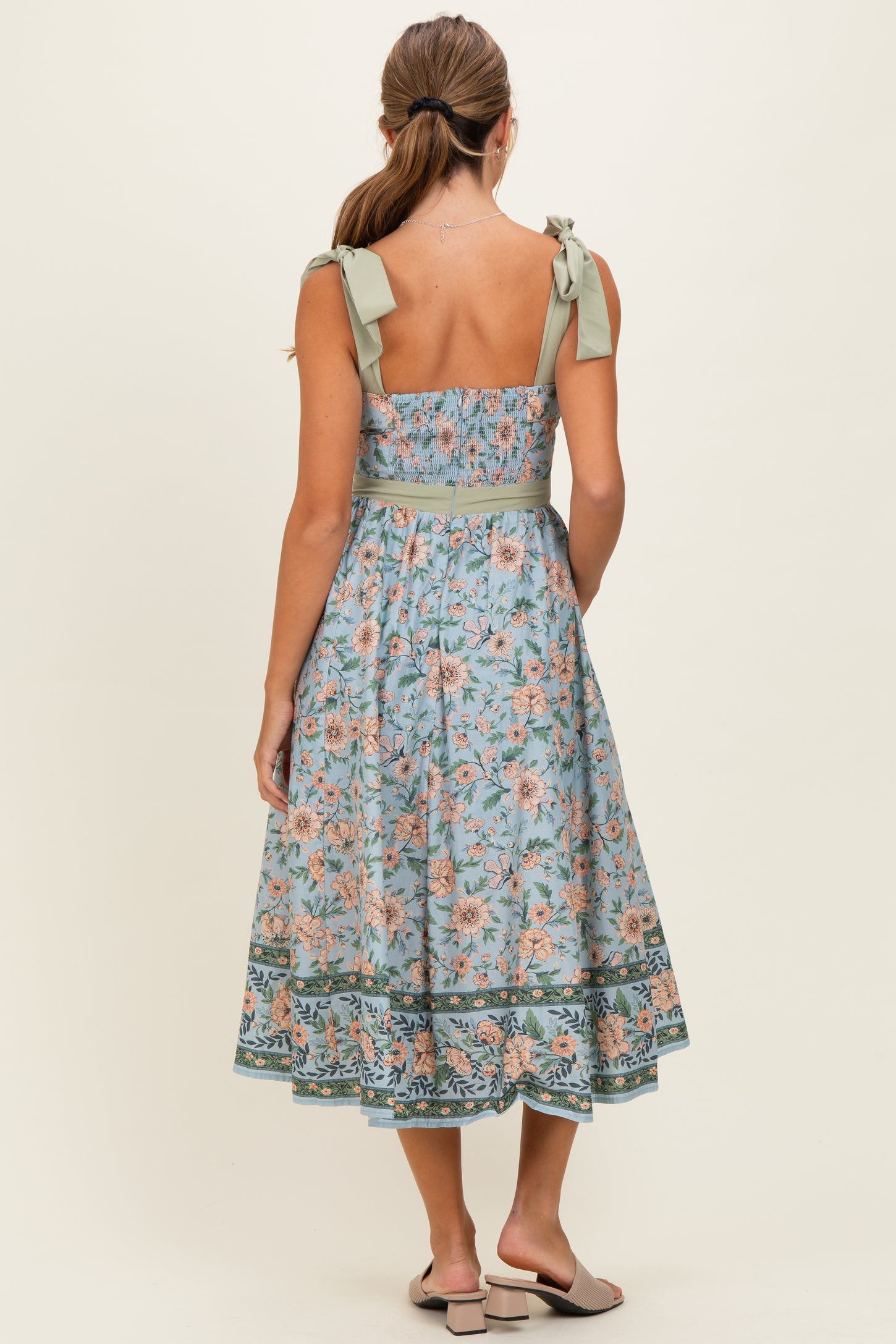 woman wearing a floral print midi dress with a fitted bodice and tie straps in soft blue and pastel colors