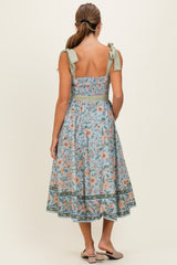 woman wearing a floral print midi dress with a fitted bodice and tie straps in soft blue and pastel colors