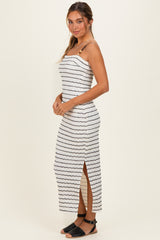 woman wearing a white striped midi dress with side slits and spaghetti straps, standing sideways against a plain background