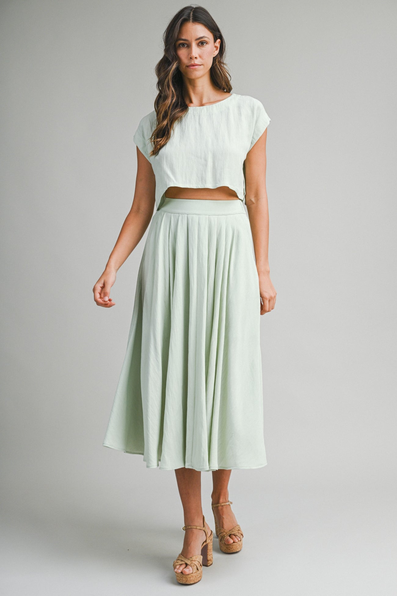 woman wearing a light green cropped top and matching pleated maxi skirt with a flowy silhouette and platform sandals