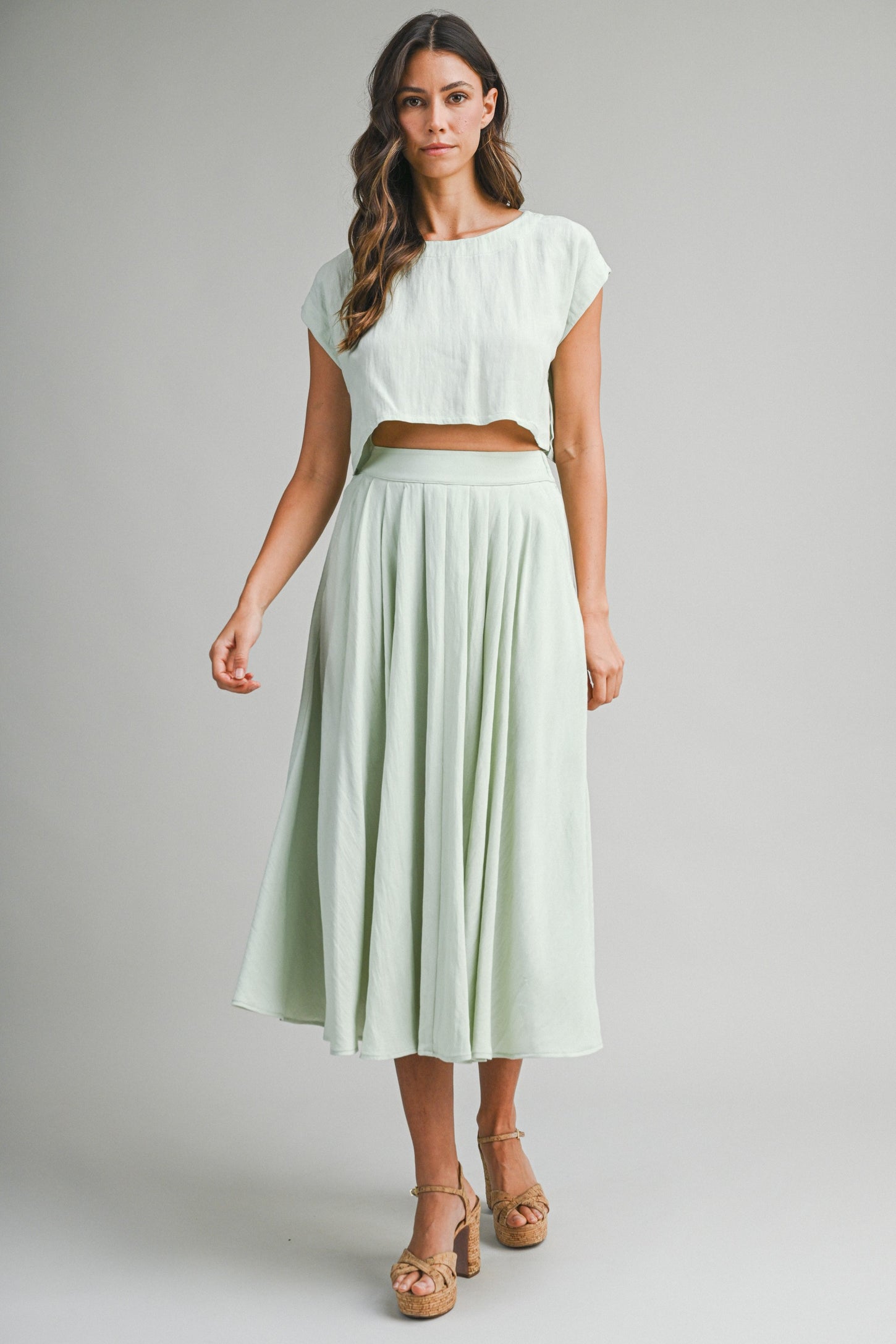 woman wearing a light green cropped top and matching pleated maxi skirt with a flowy silhouette and platform sandals