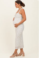 woman wearing a white floral maternity dress with lace details and holding her baby bump
