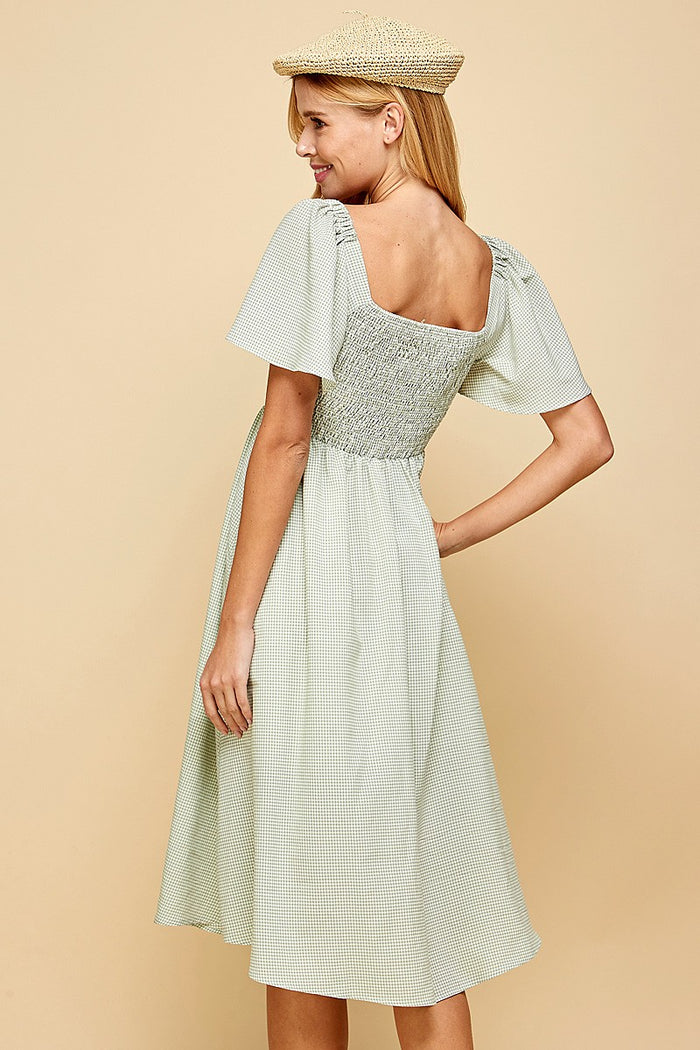 woman wearing a green gingham smocked back dress with short flutter sleeves and a midi length