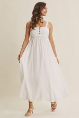 woman wearing a white maxi dress with a square neckline, button details, and spaghetti straps