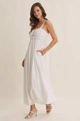 woman wearing a white maxi dress with adjustable straps, button details, and side pockets, styled with heels