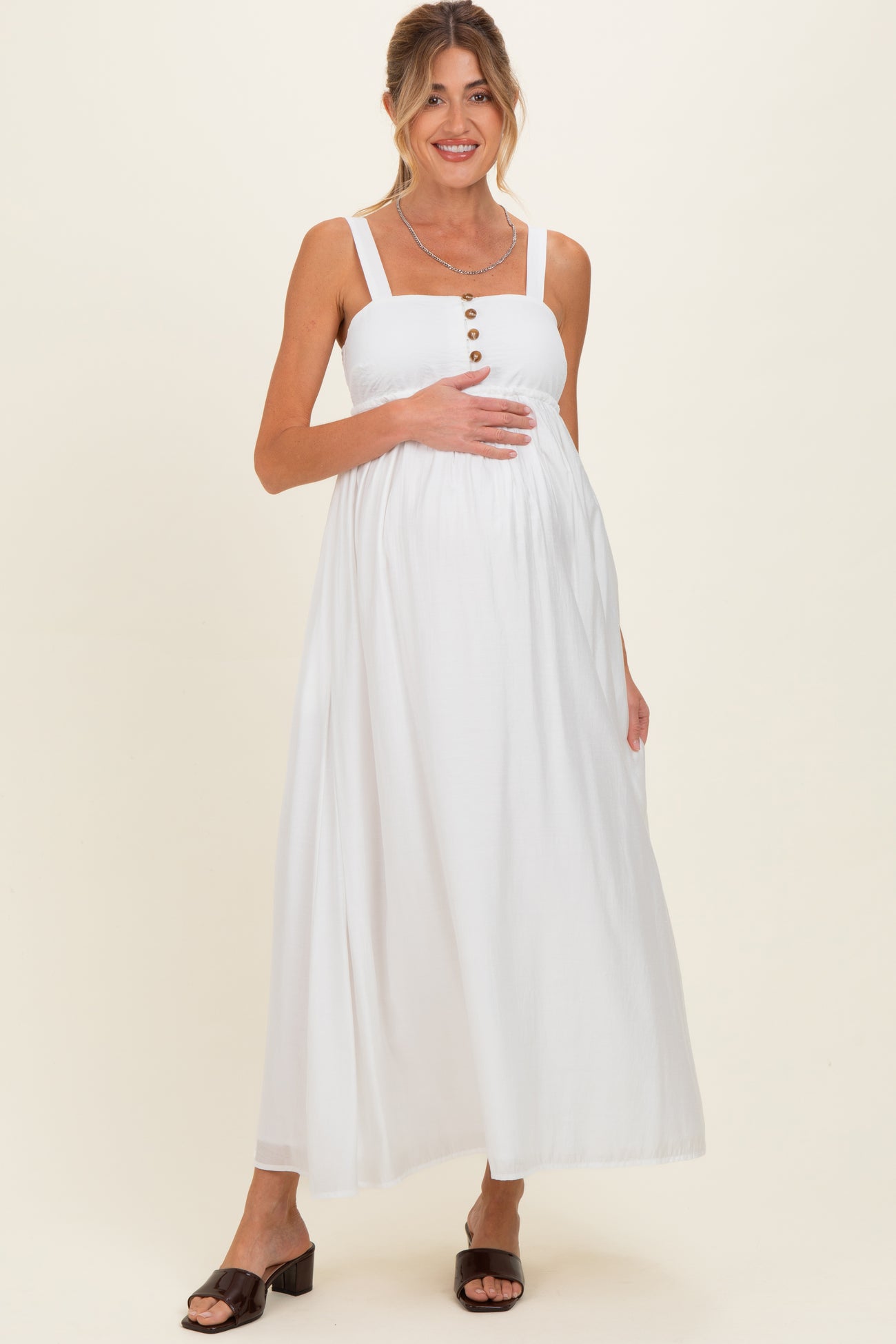 woman wearing a white maternity maxi dress with square neckline and button details, holding her baby bump