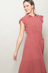 woman wearing a rust-colored ruffled sleeve shirt dress with buttons and pockets, smiling to the side