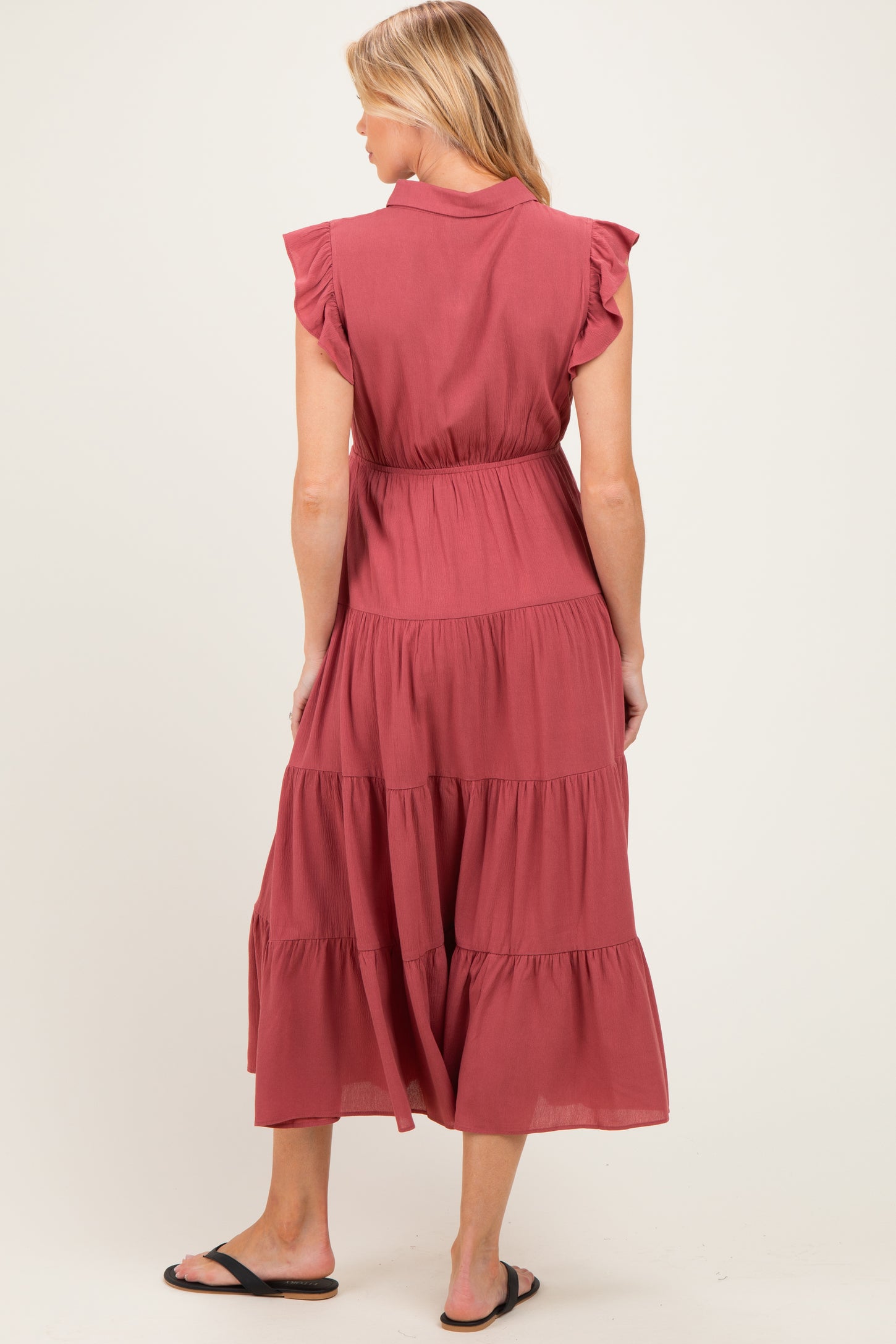 woman wearing a dusty rose maternity dress with ruffle sleeves and tiered design, showing a baby bump from the back