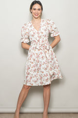 woman wearing a white floral wrap dress with puff sleeves and a tie waist, standing against a neutral background