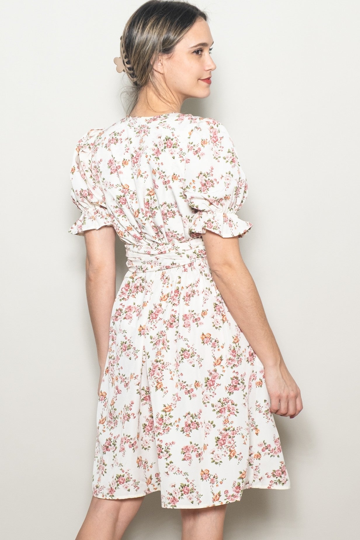 woman wearing a cream floral wrap dress with puff sleeves and a fitted waist, posed from the back