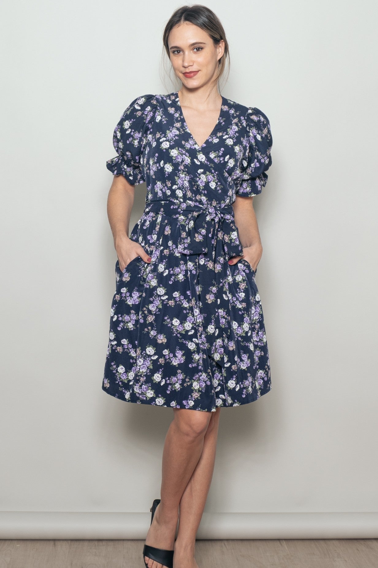 woman wearing a navy blue floral wrap dress with puff sleeves and pockets, accessorized with heels
