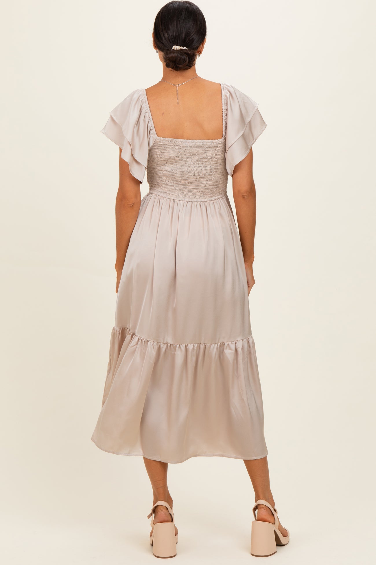 woman wearing a beige midi dress with a smocked bodice and flutter sleeves, viewed from the back