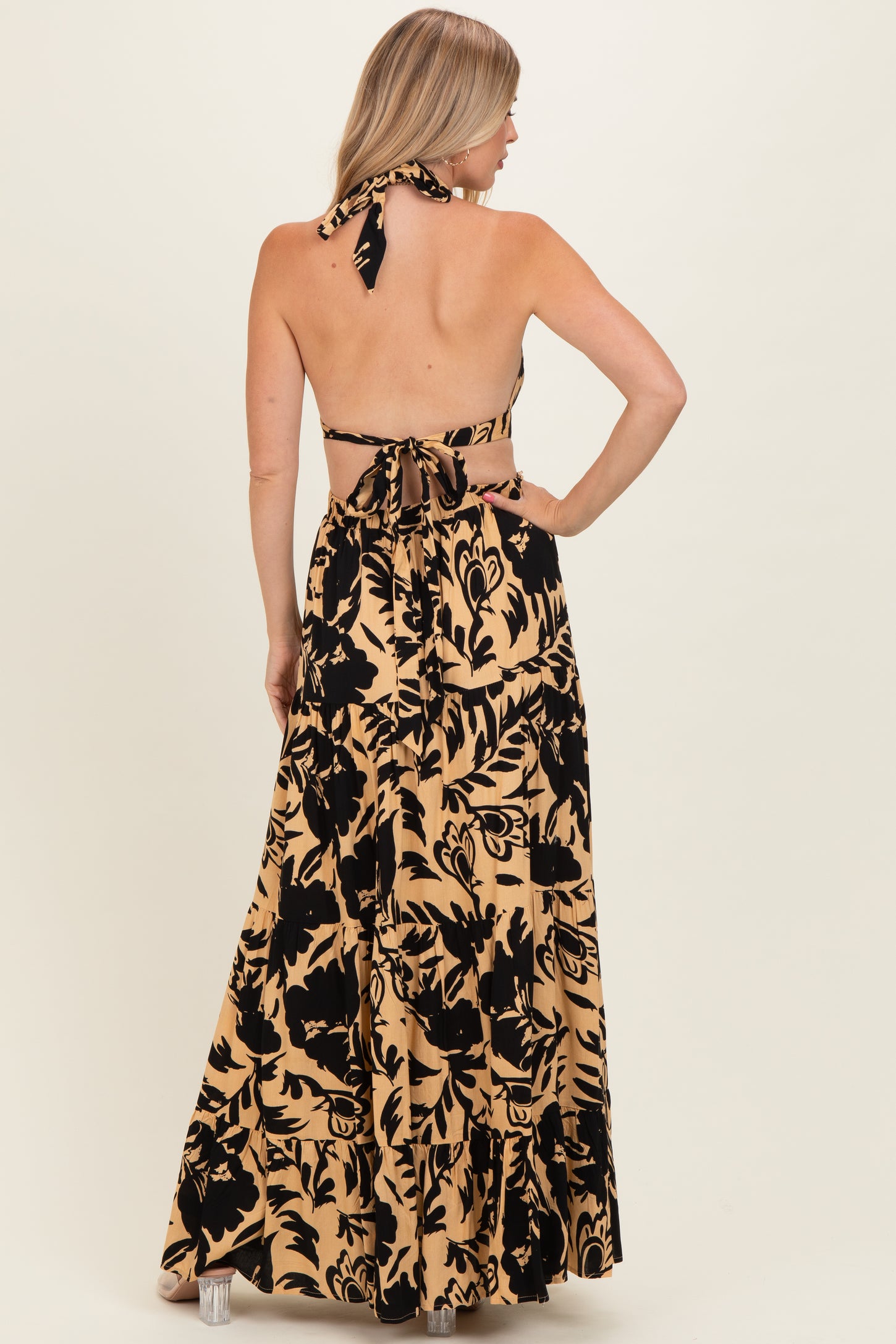 woman wearing a backless black and tan floral maxi dress with a halter neck and bow tie detail