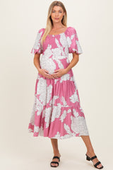 woman wearing a pink floral maternity dress with short sleeves and a smocked bodice, holding her baby bump