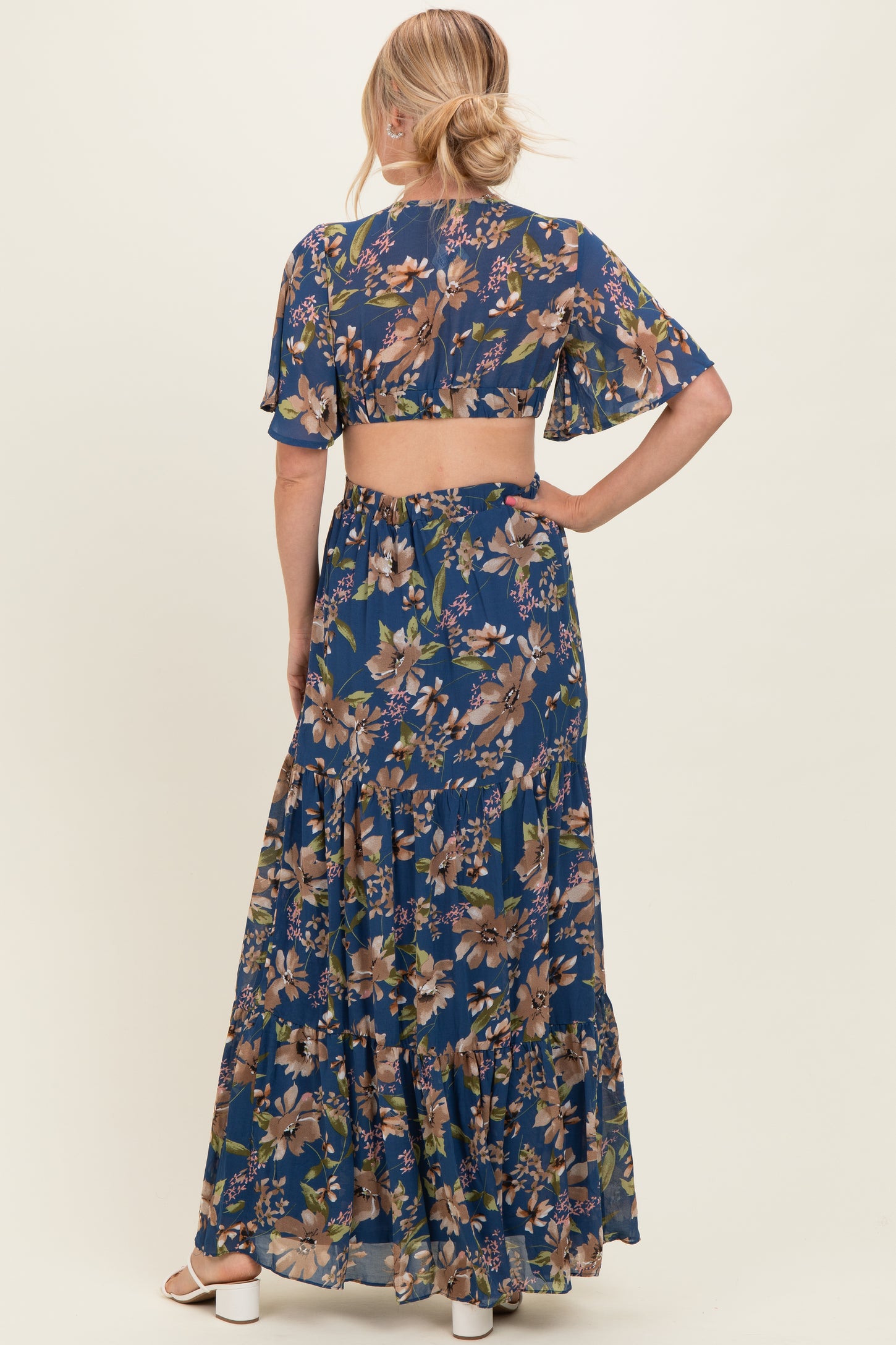 woman wearing a floral backless maxi dress with short sleeves and tiered skirt in shades of blue and earth tones
