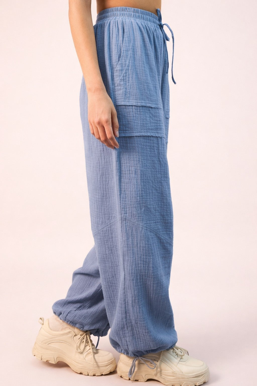 woman wearing light blue loose-fitting pants with a side pocket and drawstring waist, paired with beige sneakers