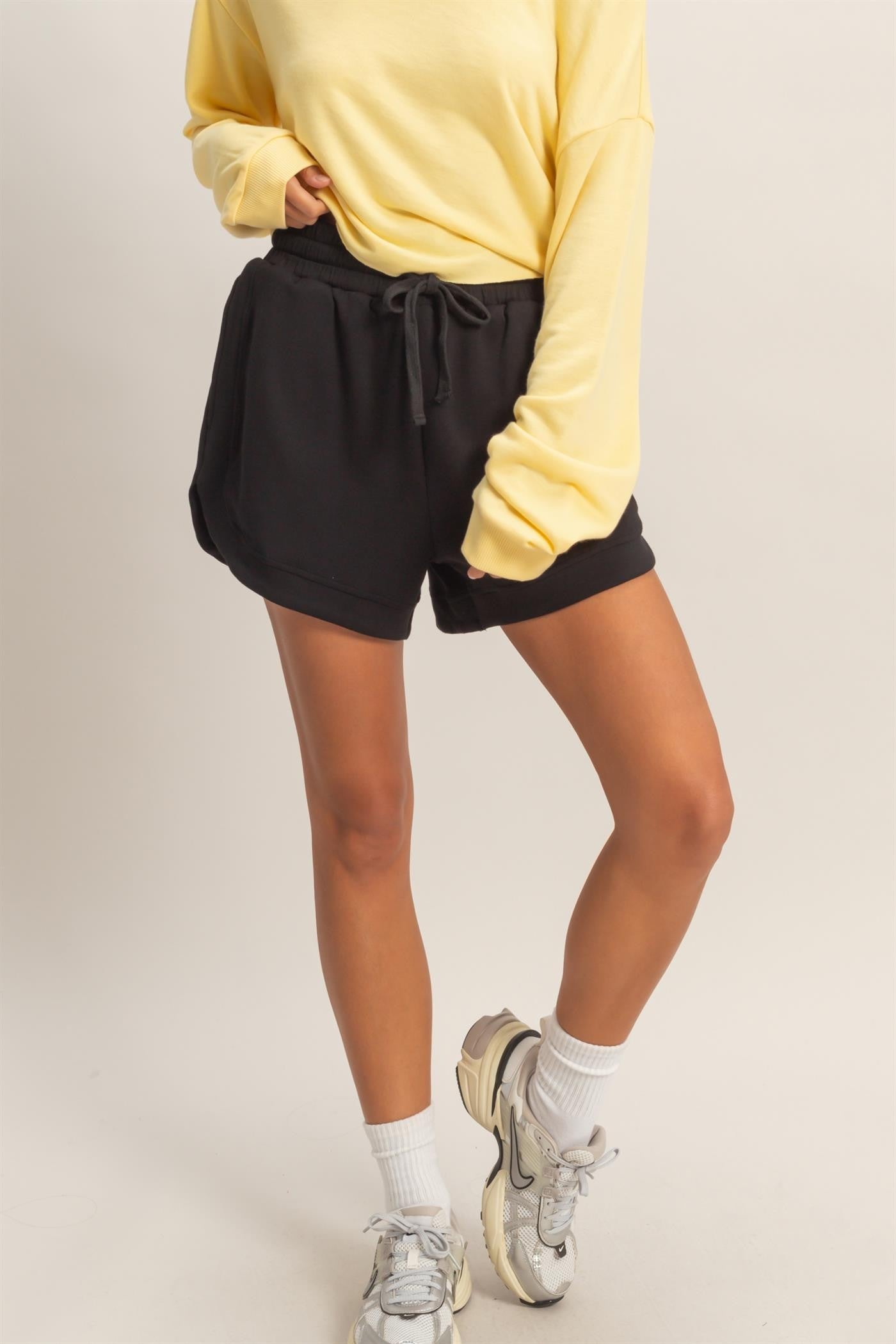 woman wearing a yellow long sleeve top and black drawstring shorts with white ankle socks and sneakers