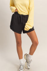 woman wearing a yellow long sleeve top and black drawstring shorts with white ankle socks and sneakers