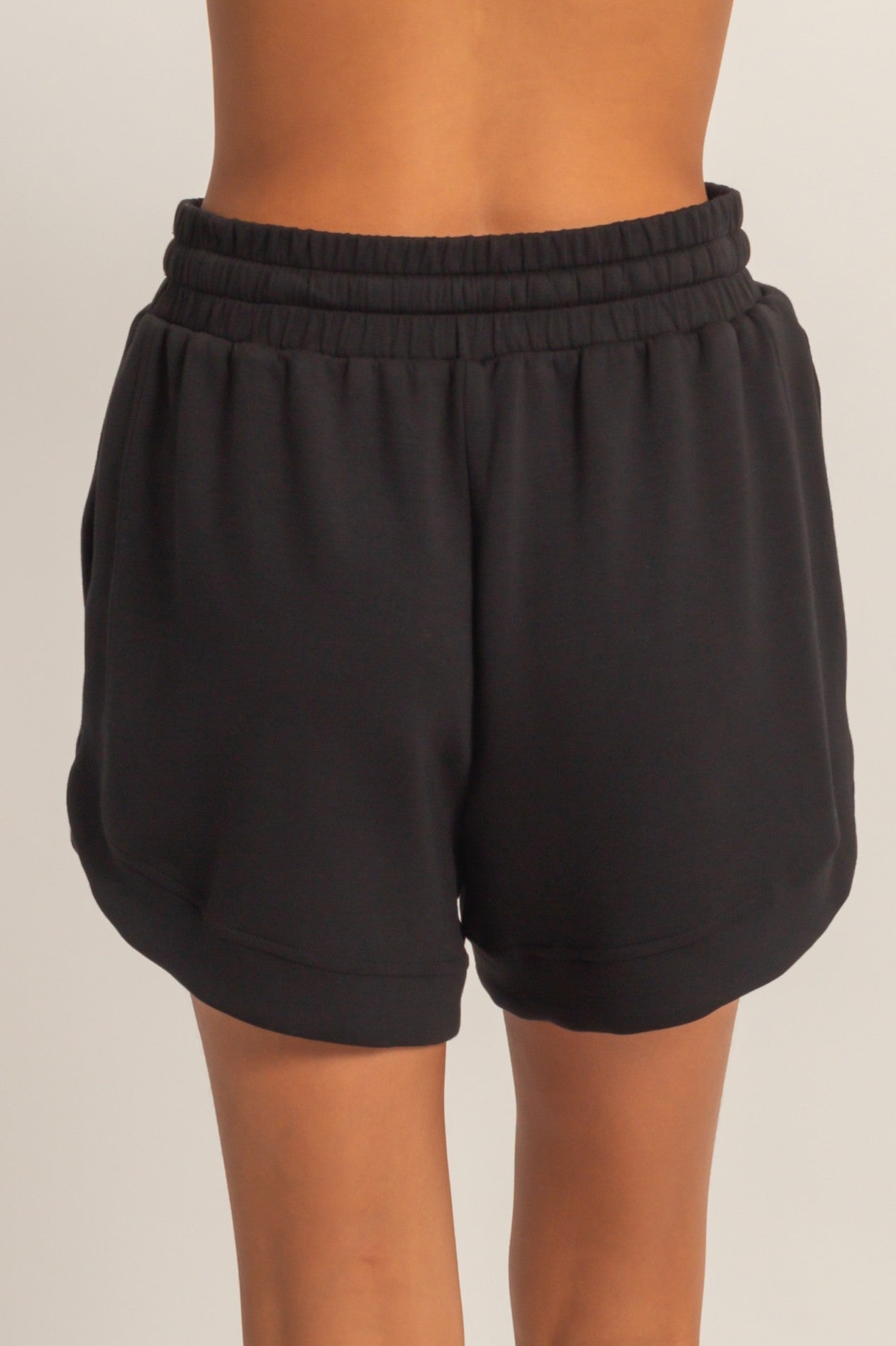 black women's athletic shorts with an elastic waistband and curved hem, shown from the back