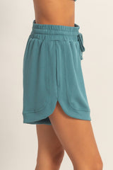 woman wearing teal drawstring shorts with a relaxed fit and side slits in a sporty style