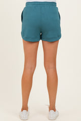 woman wearing teal maternity shorts, seen from the back, featuring a relaxed fit and side pockets