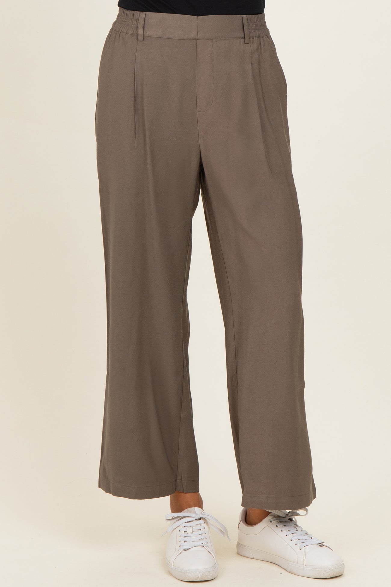 woman wearing taupe wide-leg trousers with a high waist and side pockets, paired with white sneakers