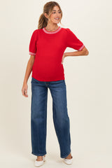 woman wearing a red maternity sweater with textured fabric and striped neckline, paired with blue wide-leg jeans and showing her baby bump
