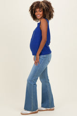 woman wearing a blue sleeveless maternity top and flared jeans, showing her baby bump