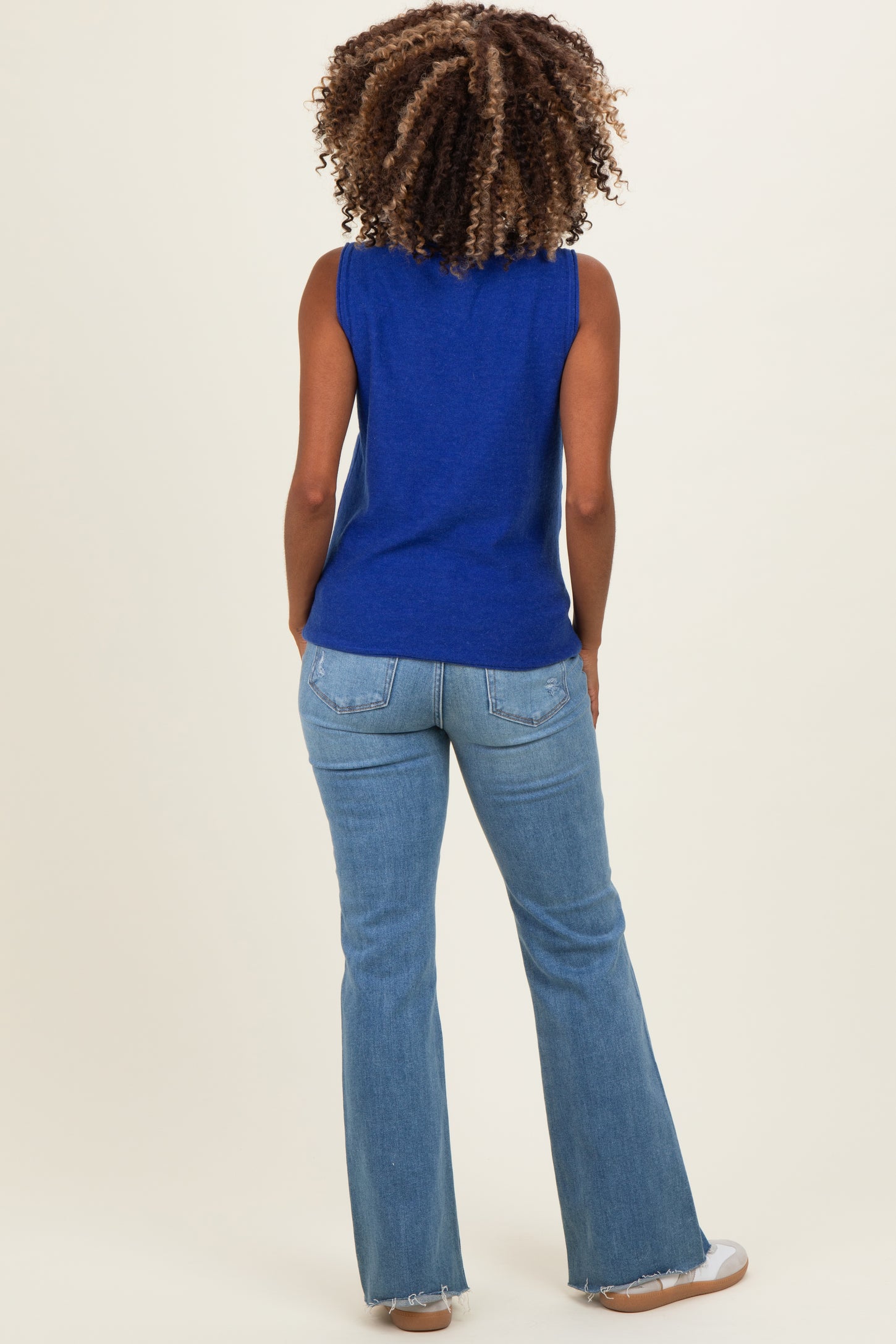 woman wearing a blue sleeveless maternity top and light blue flared jeans, showing her back and wavy hair