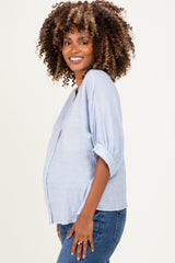 woman wearing a light blue maternity top with rolled sleeves and a visible baby bump