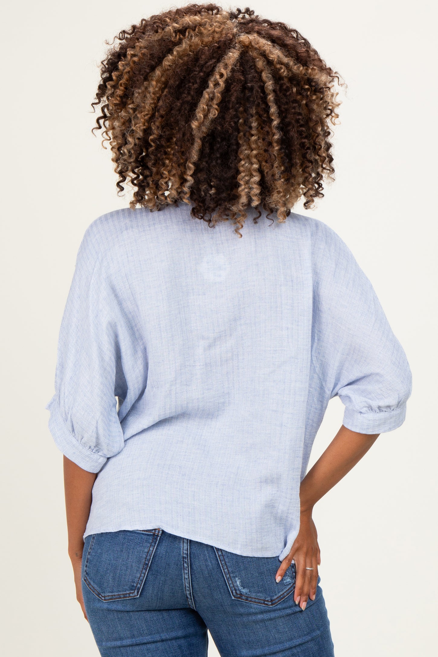 woman wearing a light blue maternity top with rolled sleeves, showcasing a relaxed fit from the back