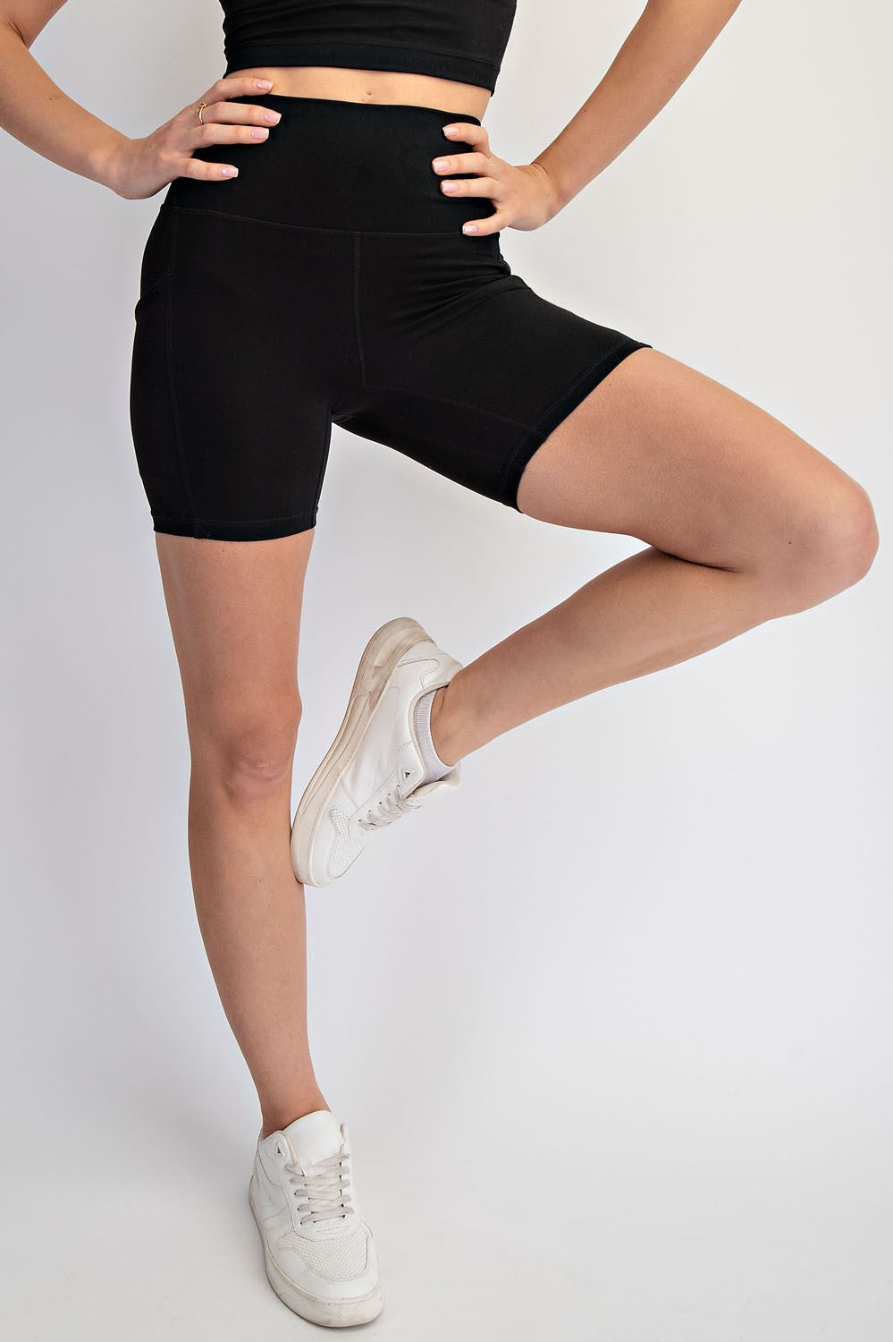 woman wearing black high-waisted athletic shorts and white sneakers, standing with one leg lifted