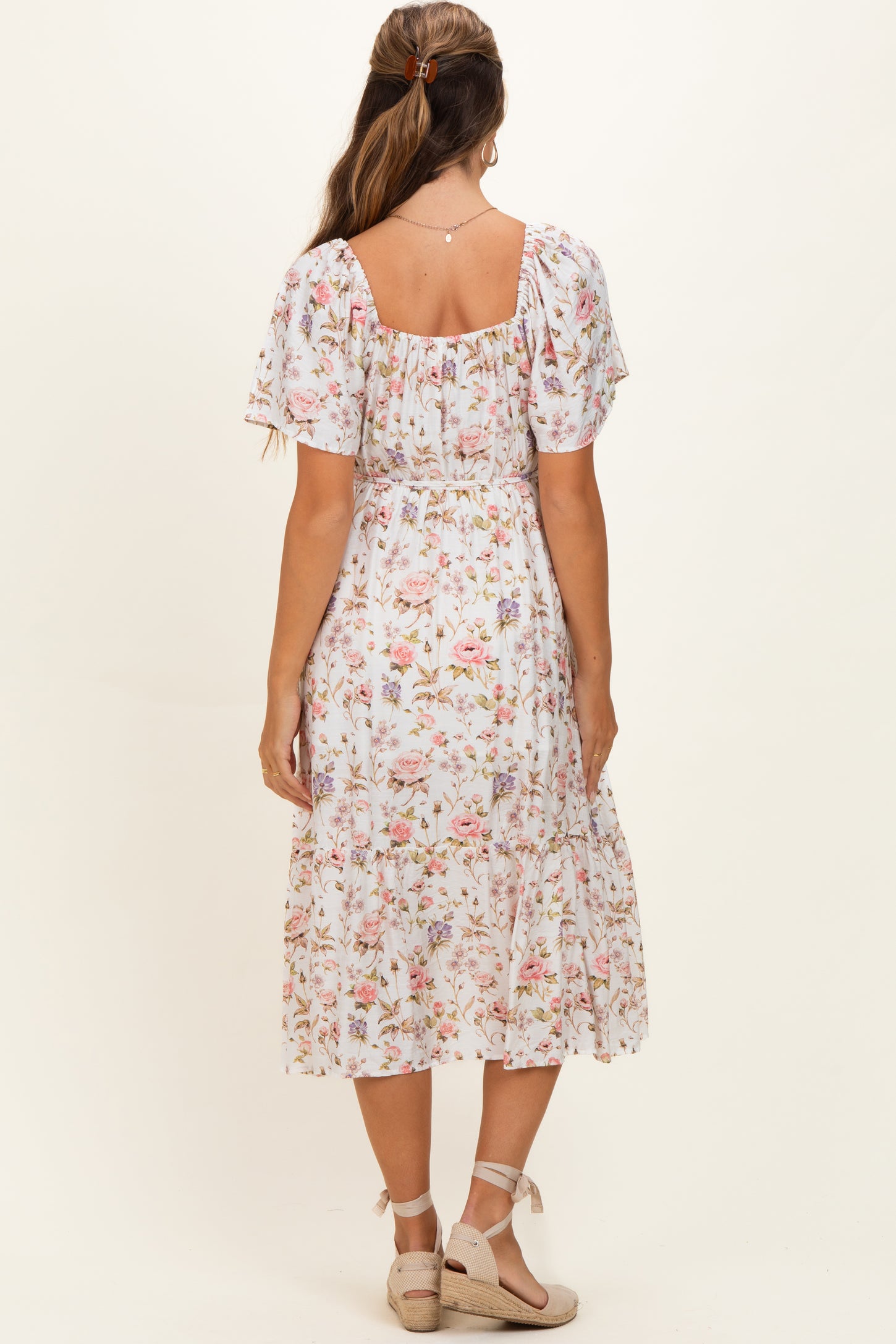 woman wearing a floral midi maternity dress with short puff sleeves and a smocked bodice, showing a baby bump