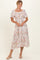 woman wearing a floral midi dress with puff sleeves and a smocked bodice, standing against a plain background