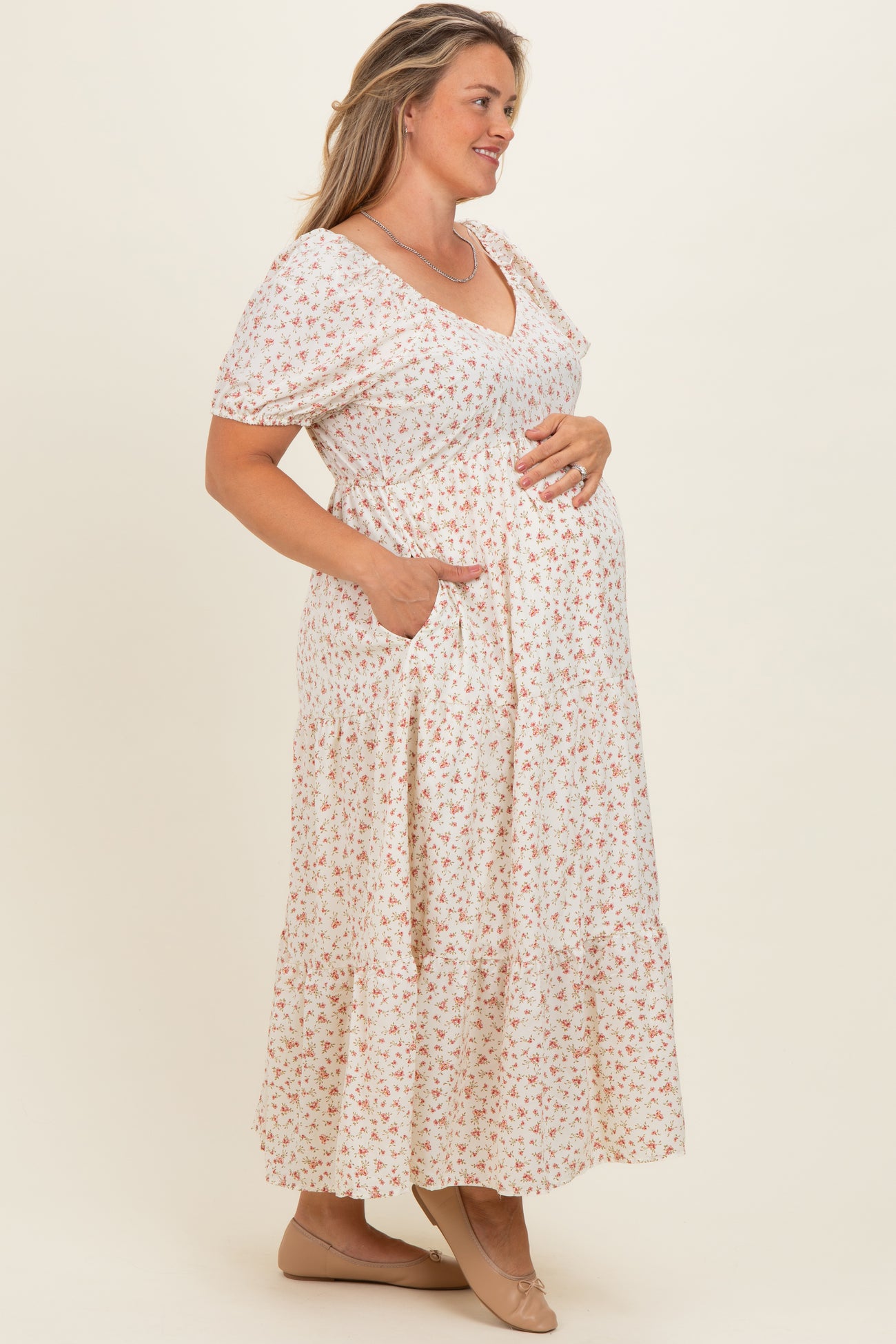 woman wearing a floral maternity maxi dress with short sleeves, v-neck, and pockets, holding her baby bump