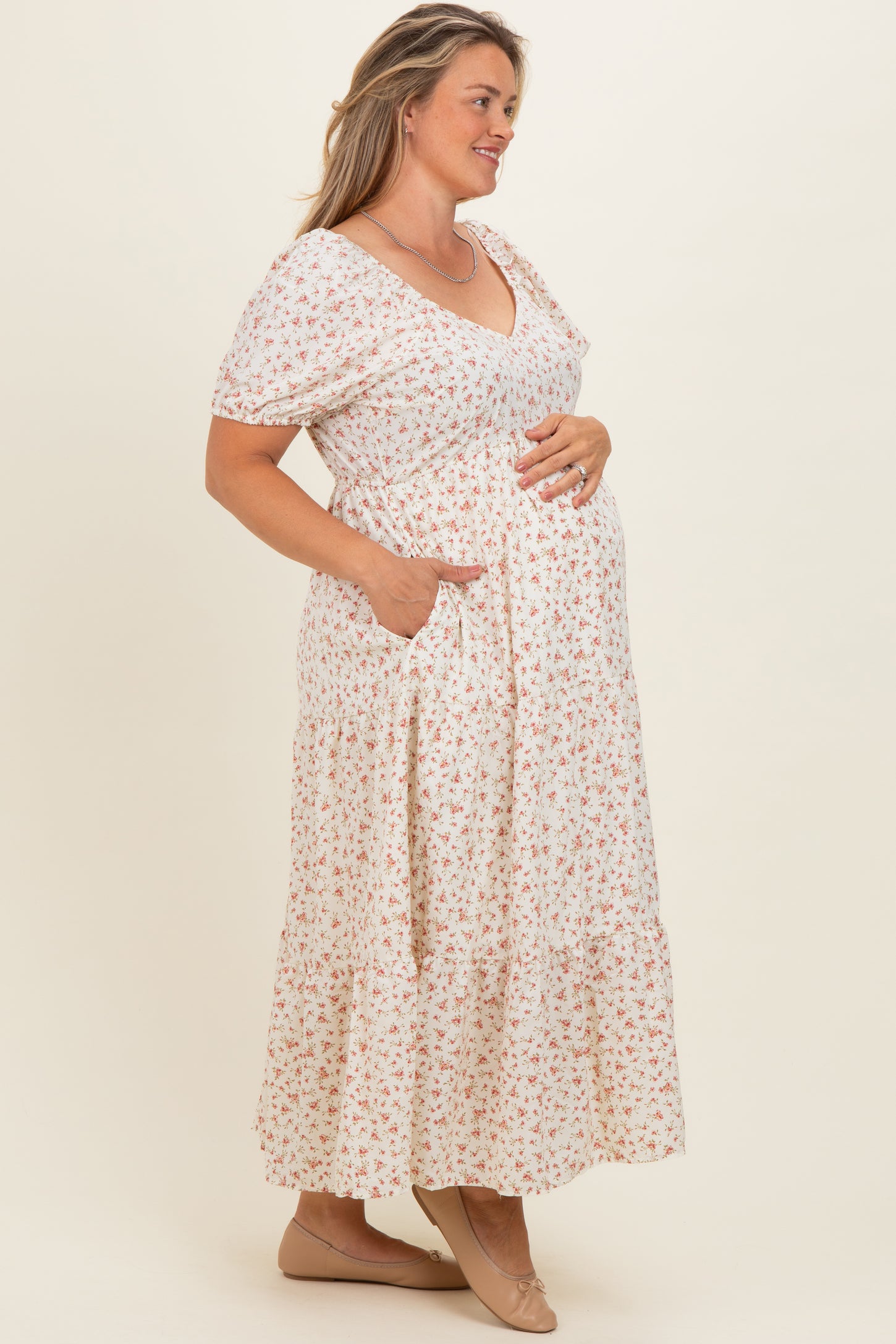 woman wearing a floral maternity maxi dress with short sleeves, v-neck, and pockets, holding her baby bump