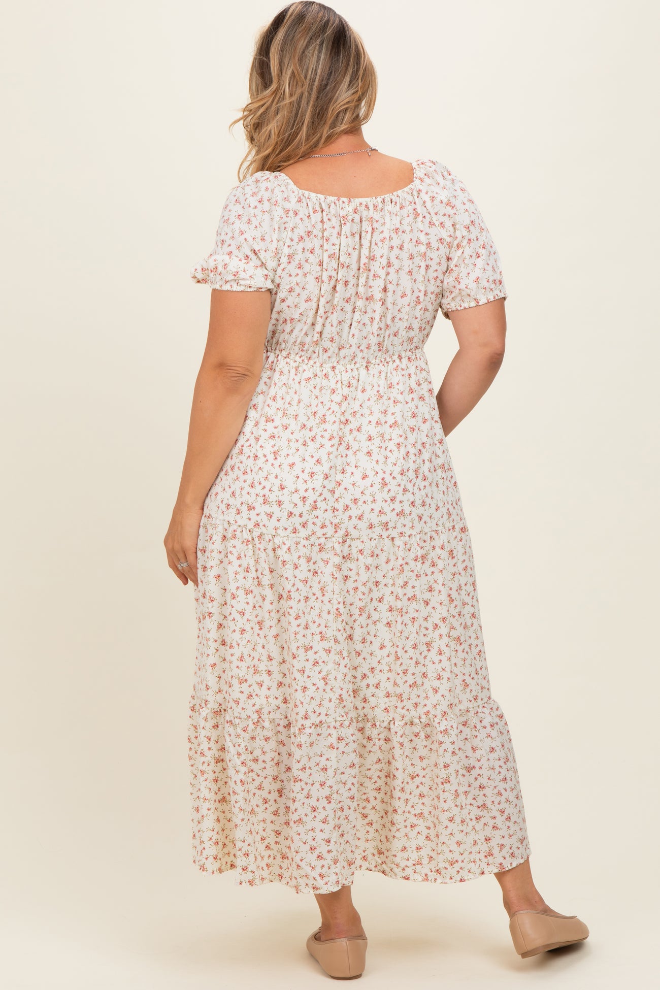 woman wearing a flowy white floral maternity plus dress with short sleeves and tiered skirt, showcasing her baby bump from the back