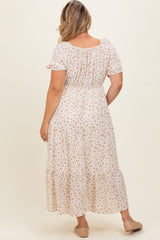 woman wearing a flowy white floral maternity plus dress with short sleeves and tiered skirt, showcasing her baby bump from the back