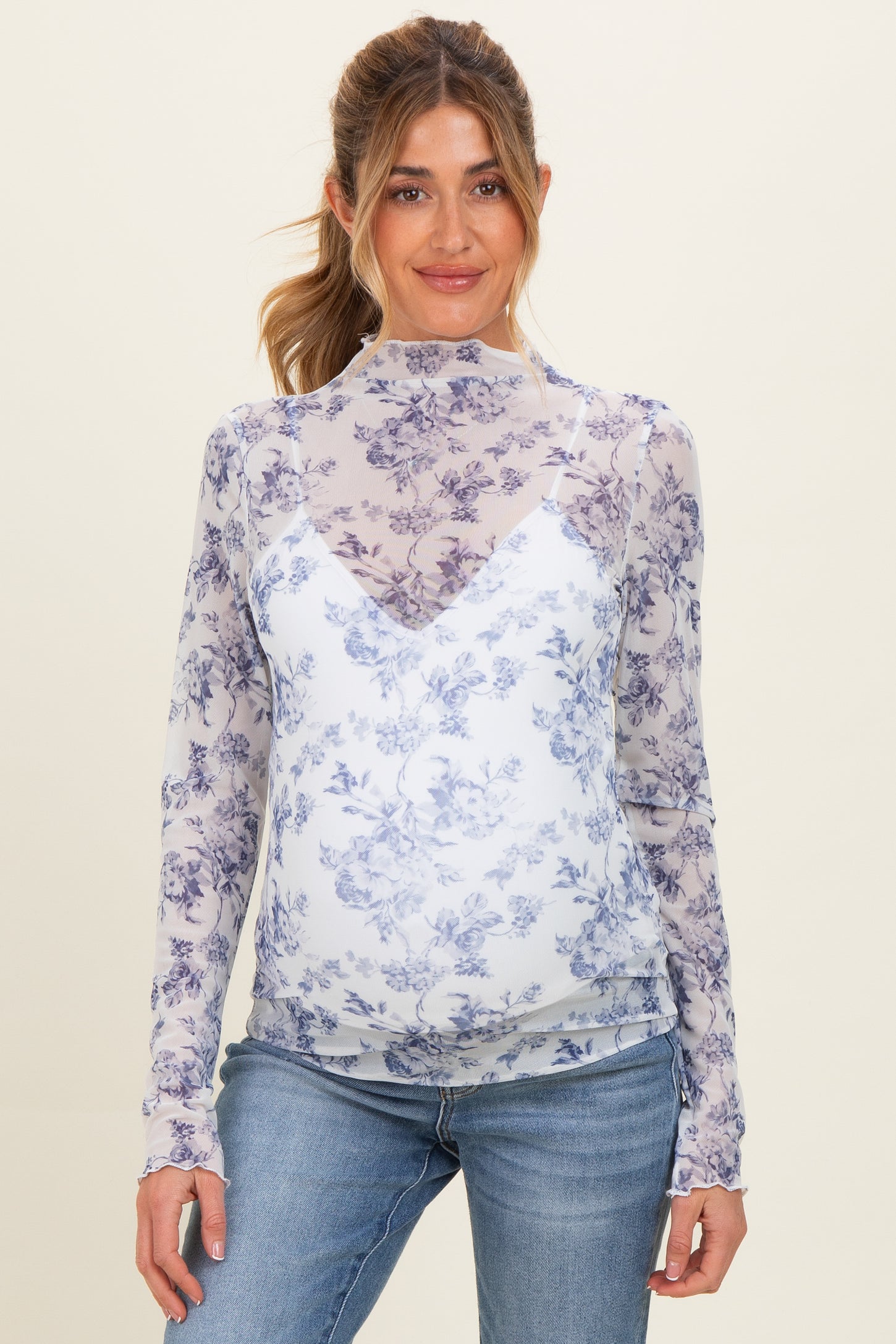 woman wearing a floral print maternity top with a sheer layer over a v-neck underneath and showing her baby bump