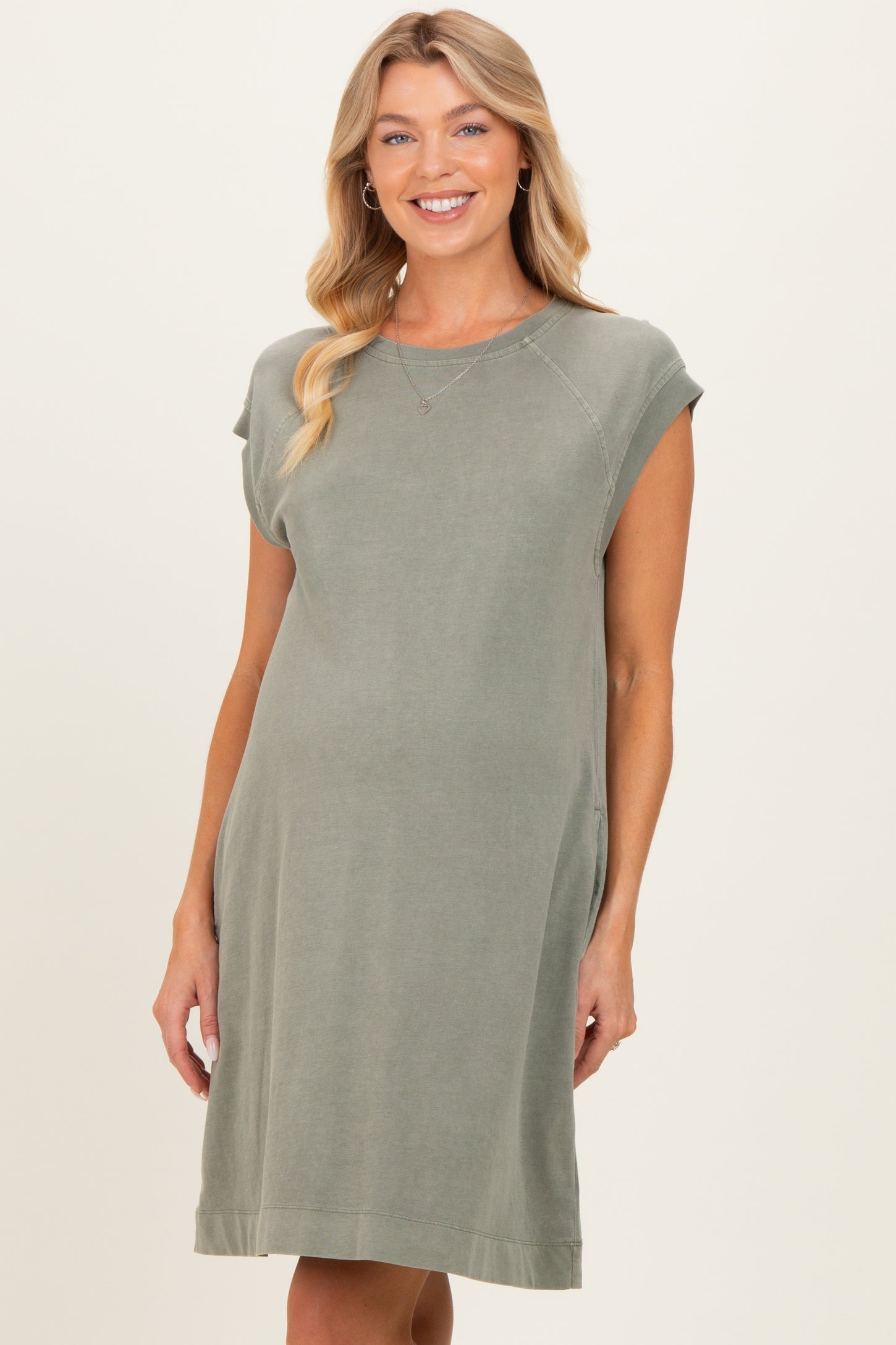 woman wearing a green cap sleeve maternity dress with side pockets and a relaxed fit showing her baby bump