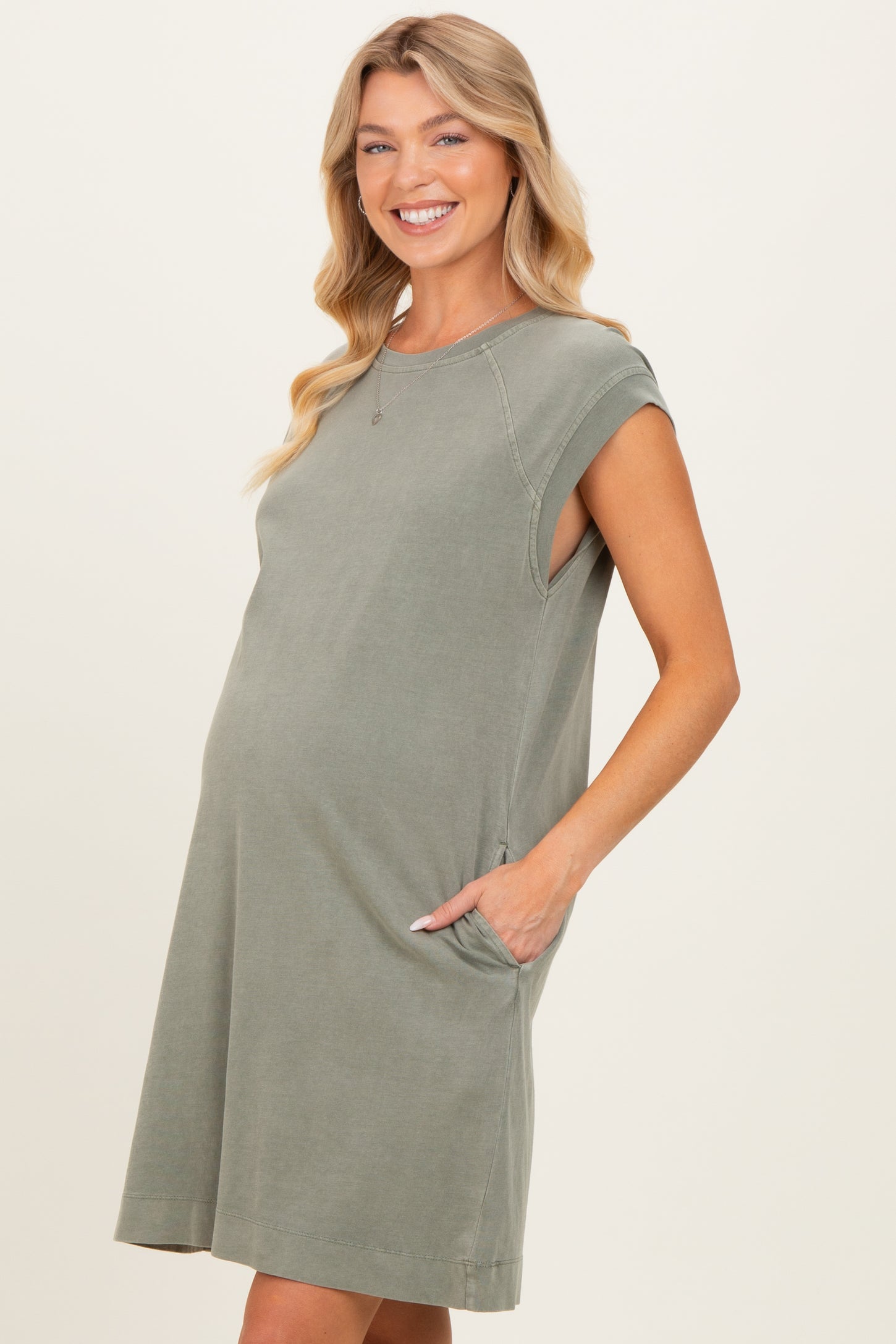woman wearing a sage green maternity dress with short sleeves and side pockets, showing her baby bump