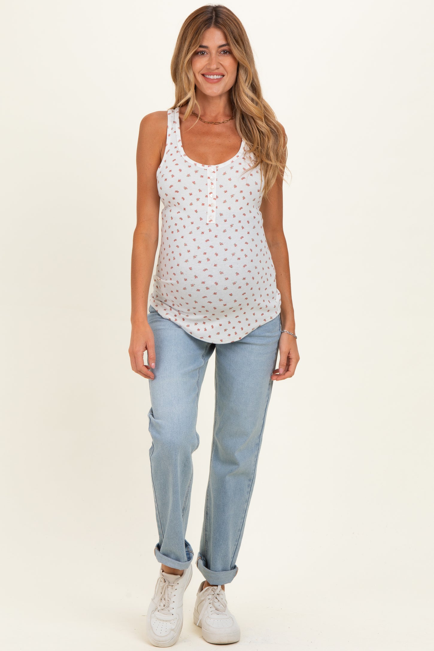 woman wearing a white maternity tank top with a floral print and blue jeans, showing her baby bump