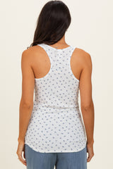 woman wearing a white tank top with a blue floral pattern, showing the back view and paired with light blue pants