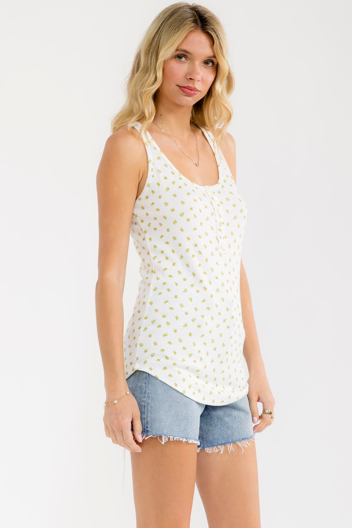 woman wearing a white tank top with yellow floral print and blue denim shorts