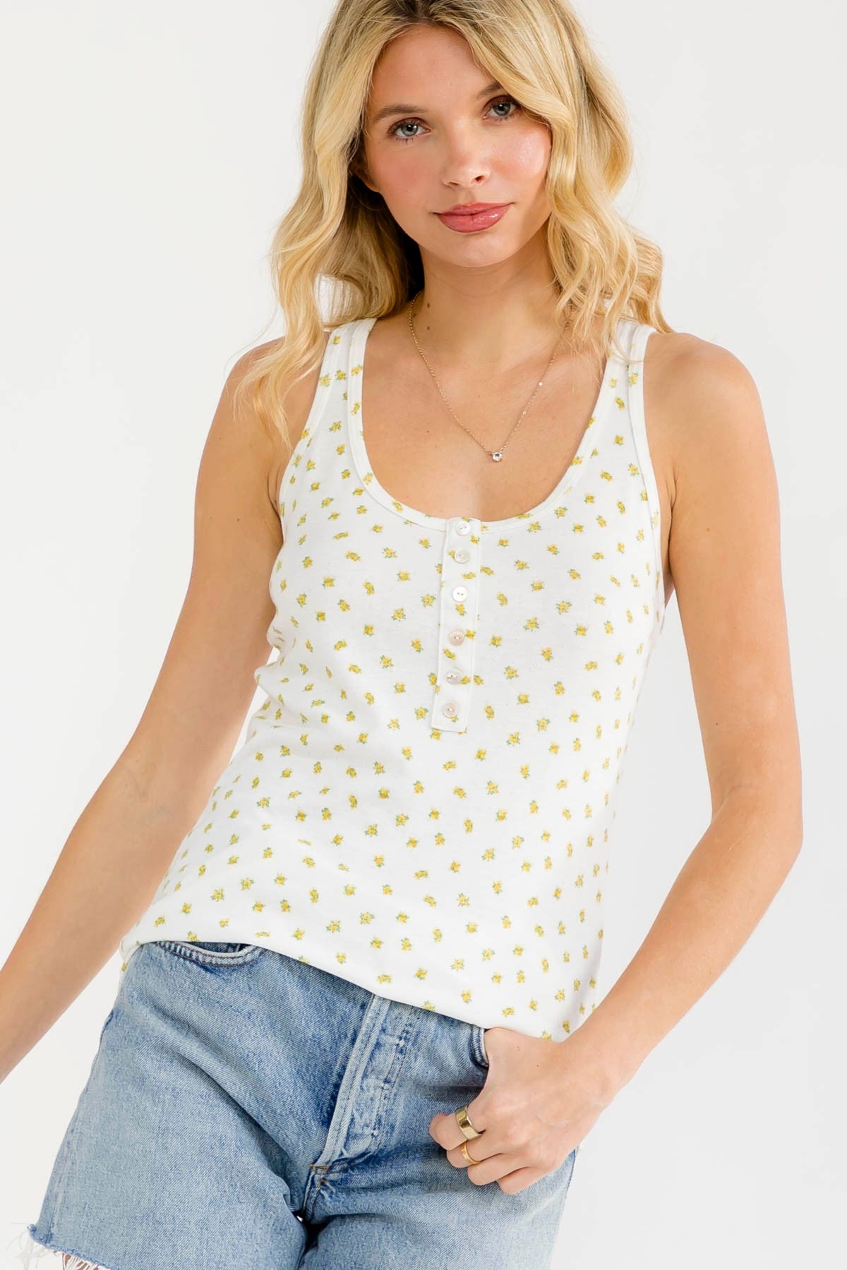 woman wearing a white floral print tank top with buttons and denim shorts