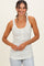 woman wearing a white tank top with small yellow floral print and buttons, smiling against a light background
