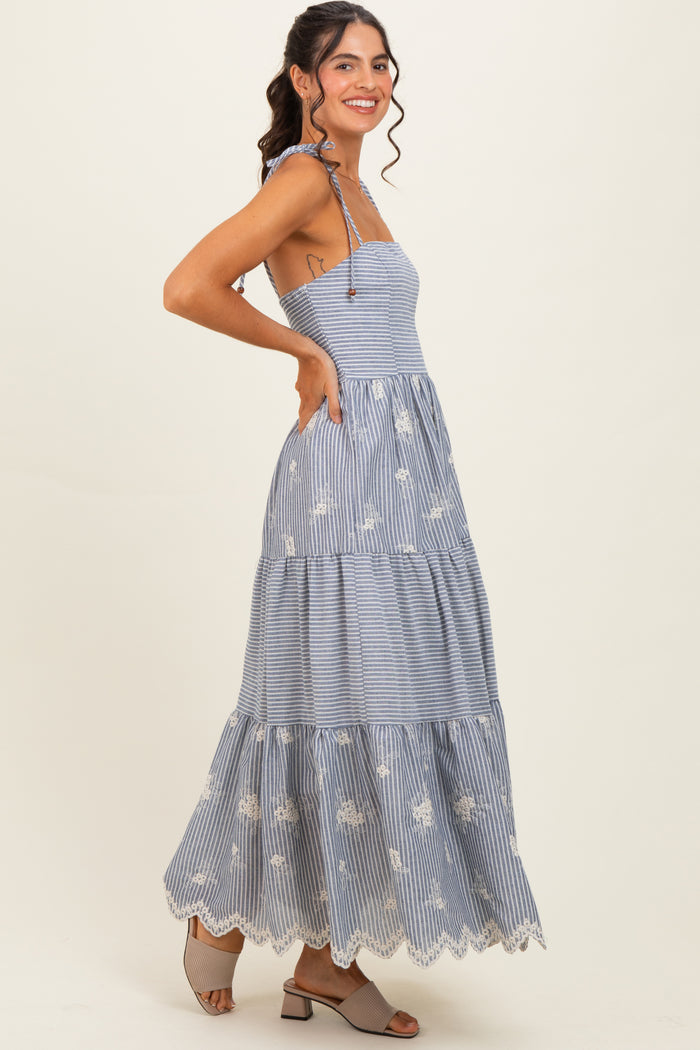 woman wearing a blue and white striped maxi dress with floral embroidery and a tiered hem, standing in profile
